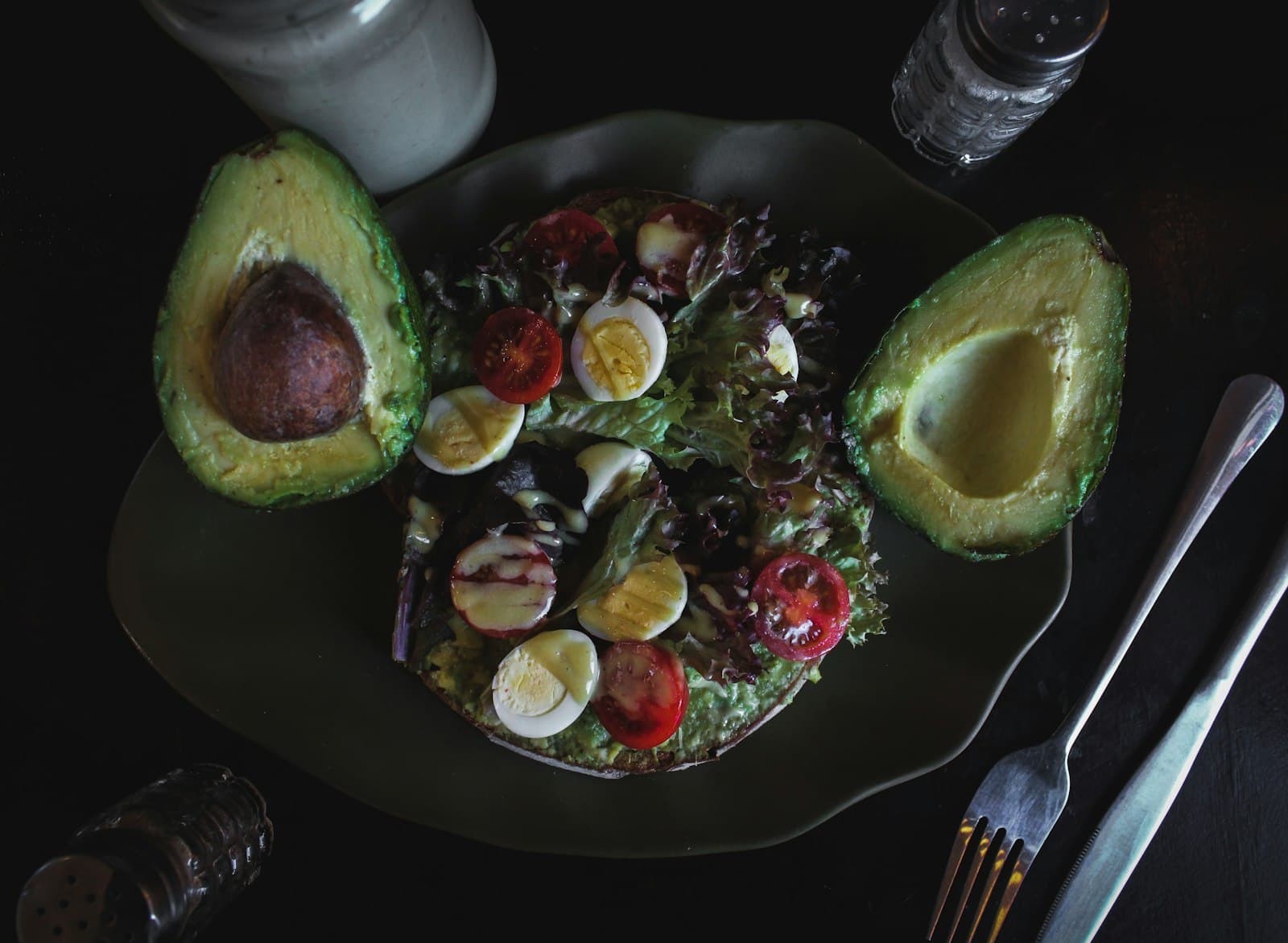 Avocado halves with quail eggs, cherry tomatoes, and mixed greens on a dark plate