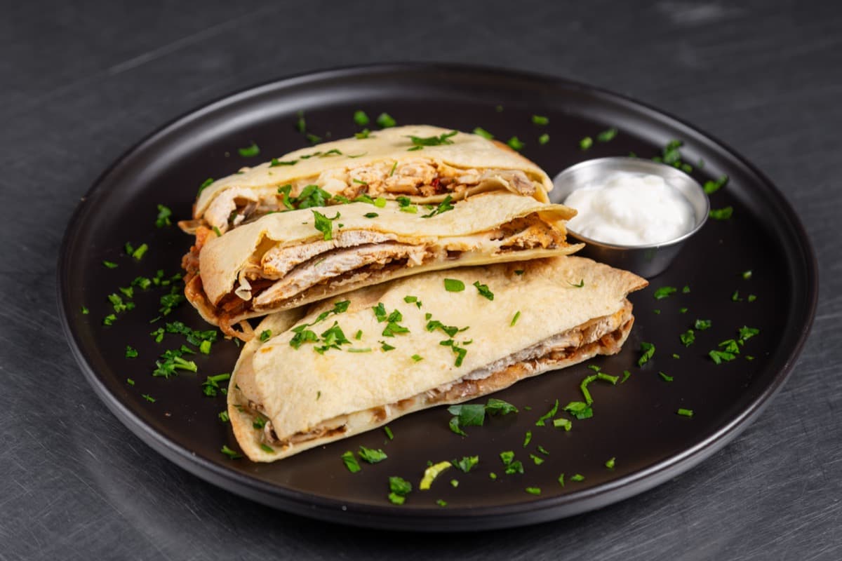 FoodieFit chicken quesadilla on a black plate with fresh herbs